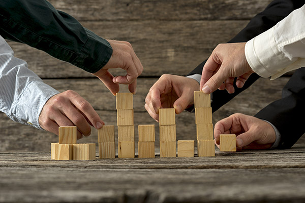 Hands of five businessman holding wooden blocks placing them into a structure. Conceptual of teamwork, strategy and business start up.